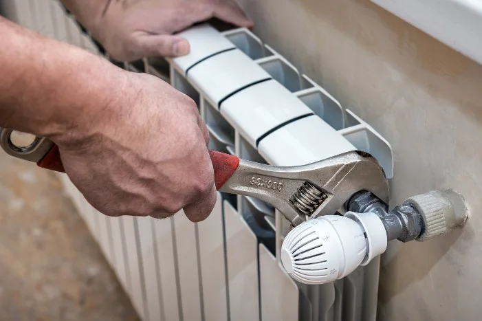 Person montiert einen Heizkörper mit Schraubenschlüssel.